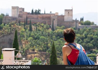 Rear view of woman looking at the Alhambra of Granada from San Nicolas viewpoint.. Rear view of woman looking at the Alhambra of Granada.