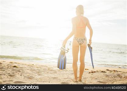 Rear view of woman on beach carrying swimming flippers