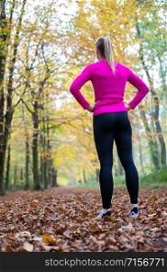 Rear View Of Woman On Early Morning Autumn Run Through Woodland Resting After Exercise