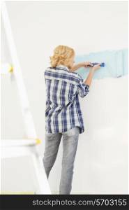 Rear view of woman painting wall with paint roller