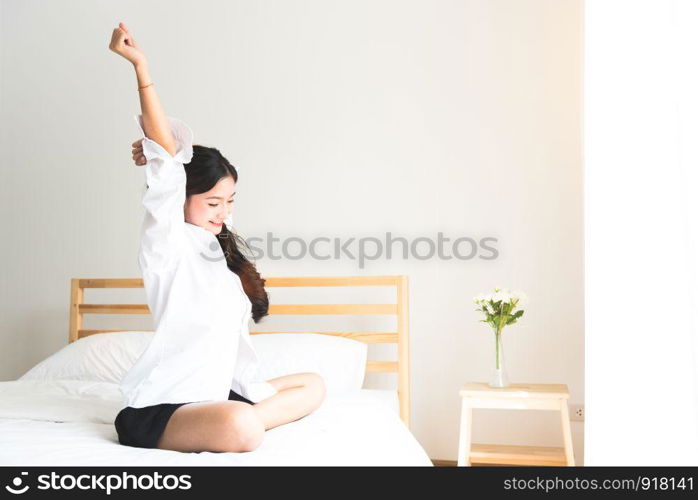 Rear view of woman stretching in morning after waking up on bed near window. Holiday and Relax concept. Lazy day and Working day concept. Office woman and worker in daily life theme