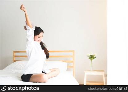 Rear view of woman stretching in morning after waking up on bed near window. Holiday and Relax concept. Lazy day and Working day concept. Office woman and worker in daily life theme