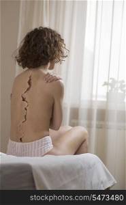 Rear view of woman with crack on back sitting in bed