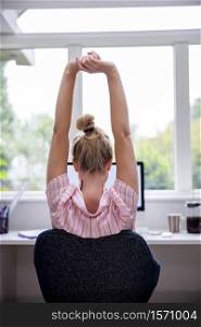 Rear View Of Woman Working From Home On Computer In Home Office Stretching At Desk