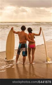 Rear view of young Asian man & woman, boy & girl, couple on a beach surfing with surfboards