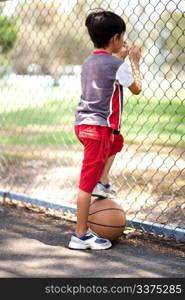 Rear view of young basketball player holding ball under his leg and and looking through fence