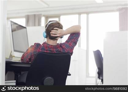 Rear view of young businessman wearing headphones at computer desk in office