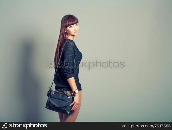 Rear view of young casual woman in pants look back on gray background, toned image. Rear view of young casual woman in pants look back