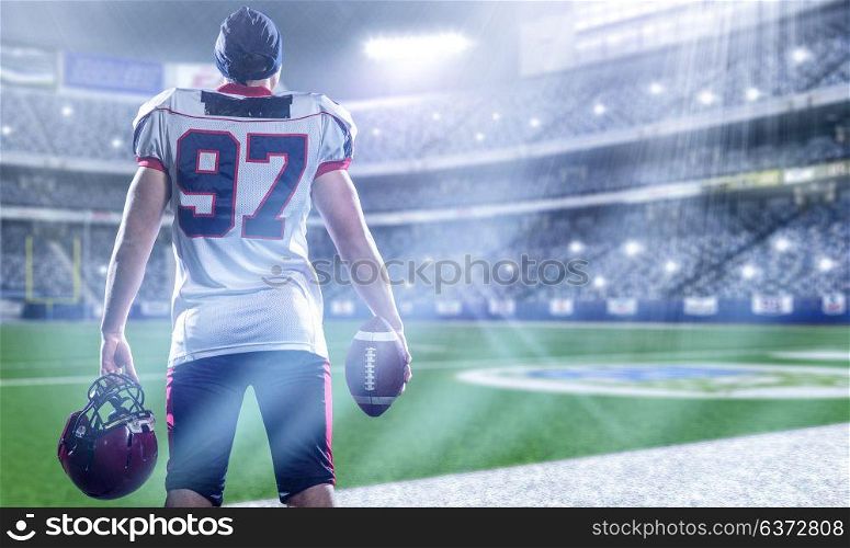 rear view of young confident American football player on the field of big modern stadium with lights and flares at night