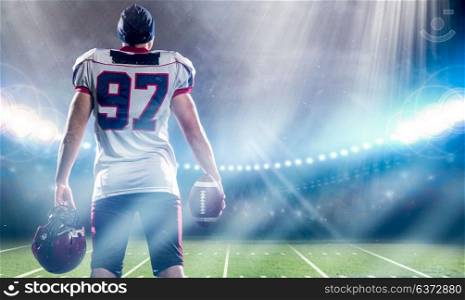 rear view of young confident American football player on the field of big modern stadium with lights and flares at night