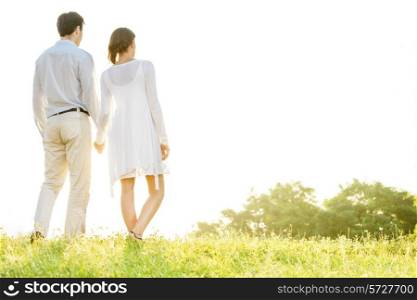 Rear view of young couple holding hands in park against clear sky