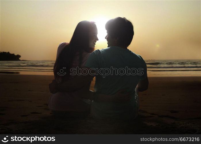 Rear view of young couple sitting together on beach at sunset