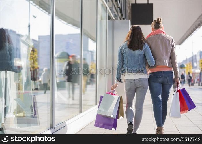 Rear view of young female friends with shopping bags walking on sidewalk by store