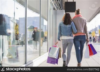 Rear view of young female friends with shopping bags walking on sidewalk by store