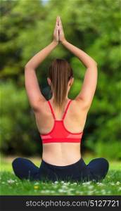 Rear view of young fit healthy woman female or girl practicing yoga pose on a mat outside in a natural tranquil green environment