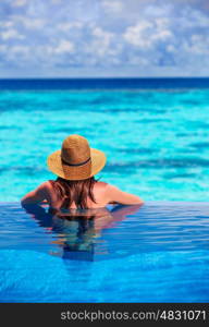 Rear view of young lady relaxing in the pool and enjoying view of beautiful seascape, refreshing in cool transparent water, summer holidays concept