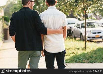 Rear view of young male couple walking on suburban sidewalk