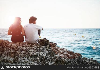 Rear view of young man and teenage sister on rocky beach, Javea, Spain