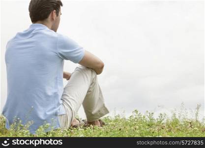 Rear view of young man sitting on grass against sky