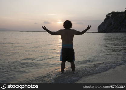 Rear view of young man with arms outstretched on beach at sunset
