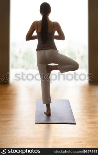 Rear view of young woman doing tree pose on yoga mat