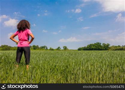 Rear view of young woman girl female runner jogger hands on hips standing in green field with blue sky