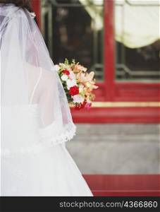 Rear view of young woman in the wedding dress holding flowers