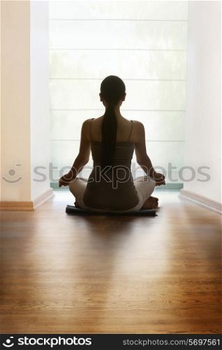 Rear view of young woman meditating on hardwood floor