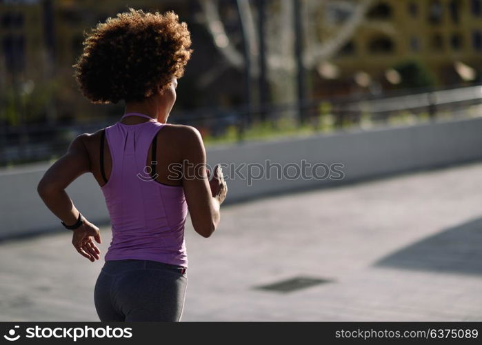 Rear view og black woman, afro hairstyle, running outdoors in urban road. Young female exercising in sport clothes at Sunset.