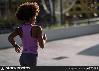 Rear view og black woman, afro hairstyle, running outdoors in urban road. Young female exercising in sport clothes at Sunset.
