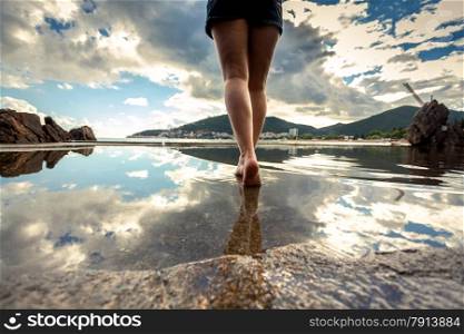 Rear view photo of beautiful slim female legs walking on water surface with reflecting sky