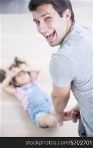 Rear view portrait of happy father dragging daughter on floor at home