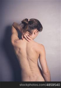 Rear view shot of a naked young woman with neck pain