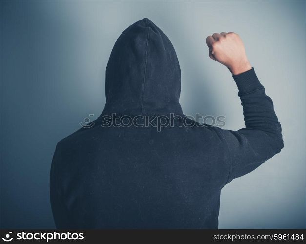 Rear view shot of a young man in a hooded top raising his fist in the air