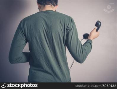 Rear view shot of a young man using a vintage rotary telephone
