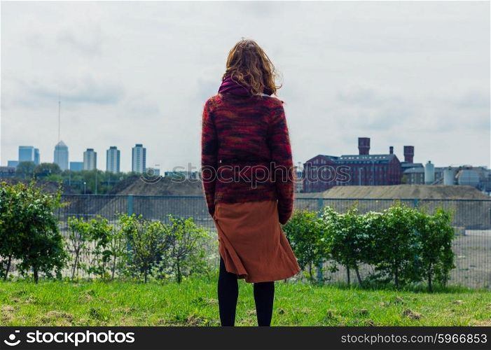 Rear view shot of a young woman standing on some grass and admiring the view of the city