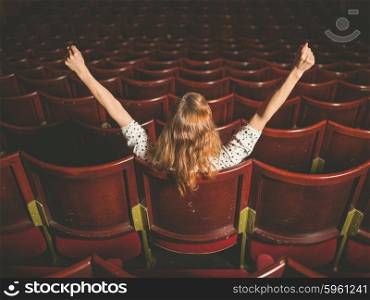 Rear view shot of an excited young woman sitting alone in an auditorium with her arms raised
