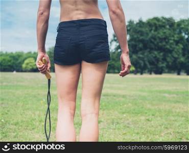Rear view shot of athletic young woman walking in the park with a jump rope in her hand