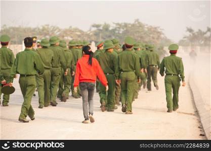 Rear view, Teen girl in red shirt walking with a group of Young Vietnamese soldier on the street, during site visit program of Vietnamese military academies at the bunker of the French General De Castries. Dien Bien Phu, Vietnam.