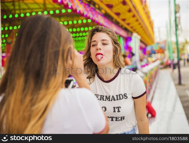 rear view woman taking her friend showing tongue amusement park