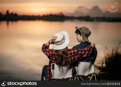 Rear view, Young Asian couple wearing trekking hat sit and enjoy the beautiful nature on sunset near the lake together during c&ing trip