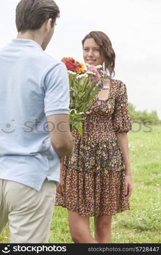 Rear view young man giving flowers to girlfriend in park