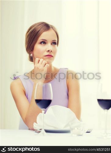 reastaurant and happiness concept - upset young woman with glass of red whine waiting for date at restaurant. upset woman with glass of whine waiting for date
