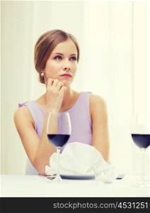 reastaurant and happiness concept - upset young woman with glass of red whine waiting for date at restaurant. upset woman with glass of whine waiting for date