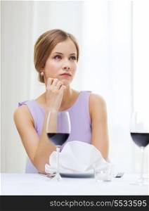 reastaurant and happiness concept - upset young woman with glass of red whine waiting for date at restaurant