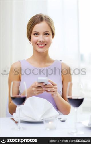 reastaurant, technology and happiness concept - smiling young woman with smartphone and glass of red wine at restaurant