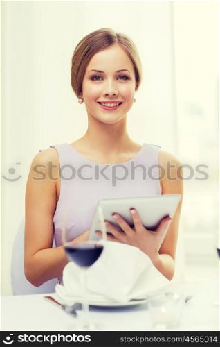reastaurant, technology and happiness concept - smiling young woman with tablet pc computer and glass of red wine at restaurant