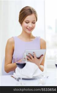 reastaurant, technology and happiness concept - smiling young woman with tablet pc computer and glass of red wine at restaurant