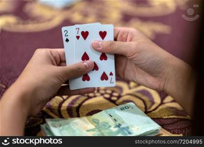 Reaw view closeup of asian woman playing card with money on the table over the carpet, risk and luck game concept
