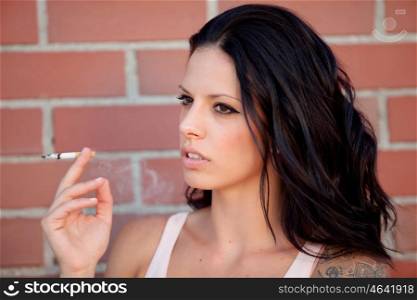 Rebel brunette woman with tight shirt smoking a cigarette on background of red bricks